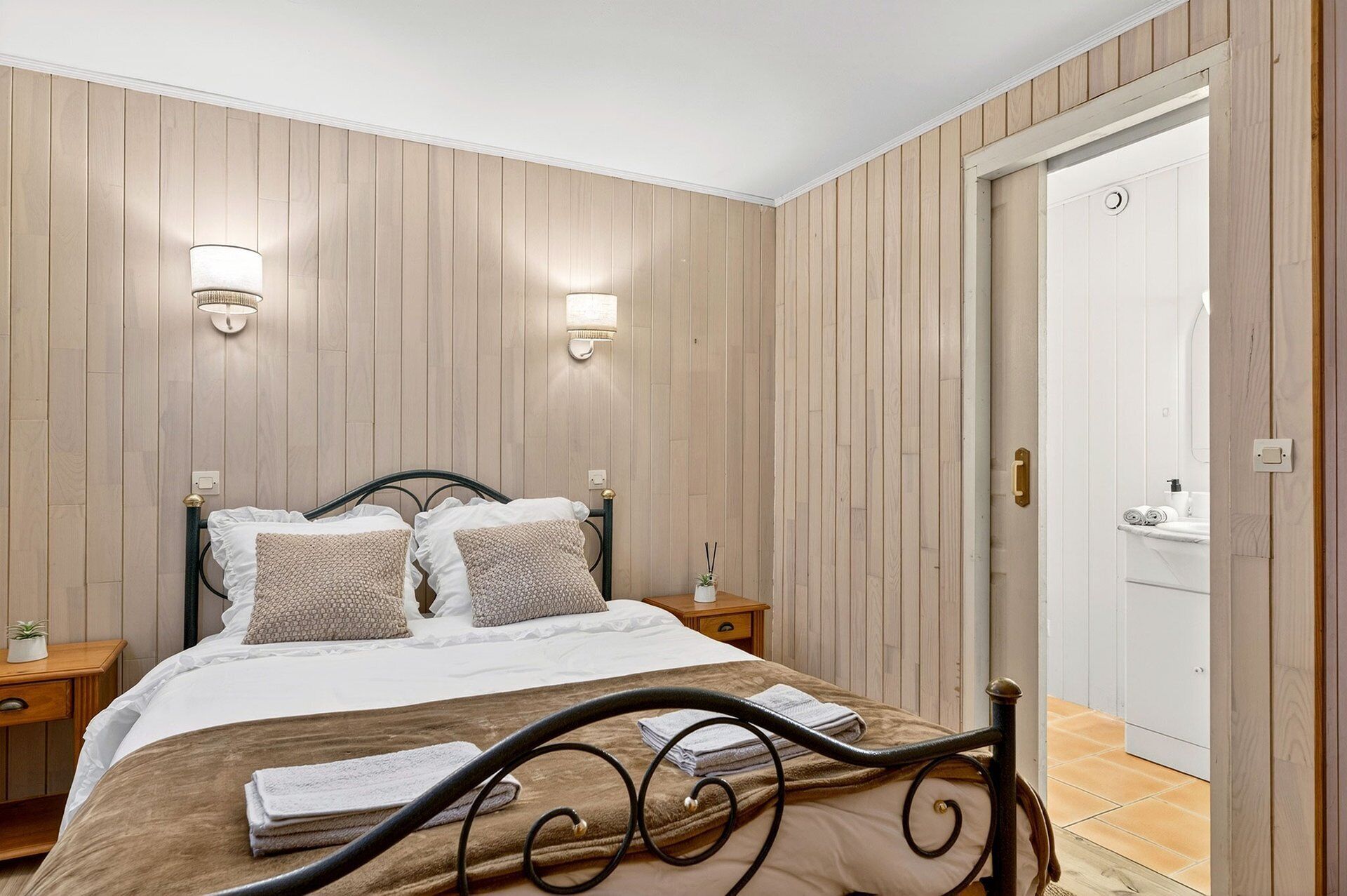 Um quarto com uma cama, mesas de cabeceira, um relógio na parede e uma porta.