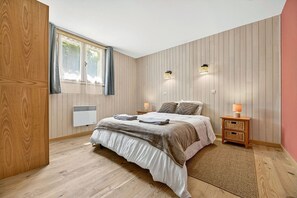 Ein Schlafzimmer mit einem Bett, zwei Nachttischen, einem fensterbelaubten Fenster und Wandleuchten sowie einem Wandheizgerät.