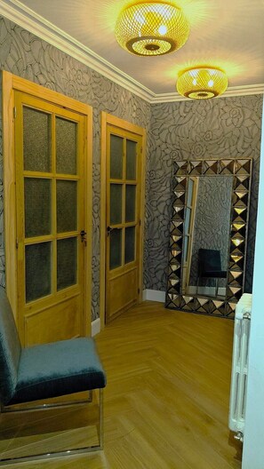 Une pièce dotée de deux portes en bois, d’un miroir aux motifs géométriques, d’un banc et d’un radiateur.
