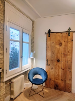 Une pièce avec une grande fenêtre, une chaise bleue, une porte en bois et un radiateur.