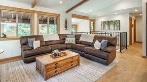 Un salón amplio con un gran sofá de cuero marrón en forma de L, una mesa de centro de madera y una escalera que sube a un nivel superior.