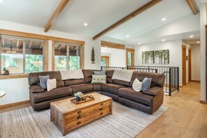 Ein geräumiges Wohnzimmer mit einem großzügigen, lederbezogenen L-Sofa in Braun, einem Holztisch und einer Treppe, die zu einer oberen Ebene führt.