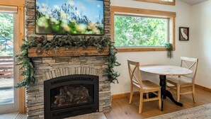 Una chimenea de piedra con un televisor encima, una mesa de comedor con sillas y una ventana con vistas a árboles.
