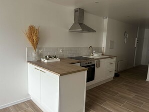 A modern kitchen with white cabinetry, a central island, a stainless steel range hood, and a backsplash.