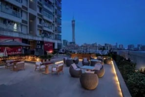 Eine Dachterrasse mit Außenbestuhlung, Blick auf eine Stadtlandschaft und ein hoher Turm im Hintergrund.