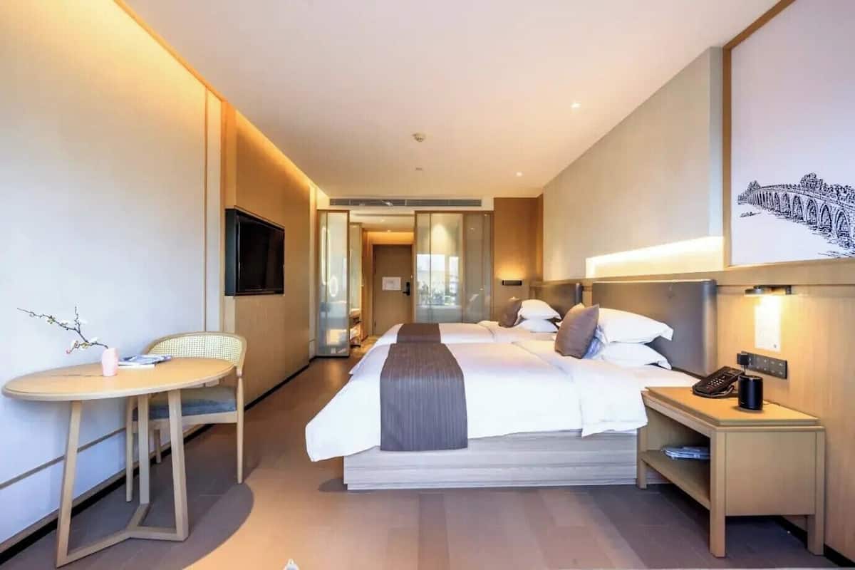 A hotel room with a large bed, a desk, a chair, a TV, and a wall-mounted phone.