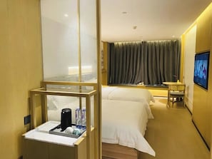 Habitación de hotel con cama, una mesita con una silla, televisión y ventana con cortinas.
