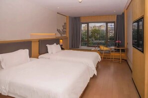 Habitación de hotel con dos camas, una mesita, una silla, un ventanal con vistas a edificios y un adorno en la pared.