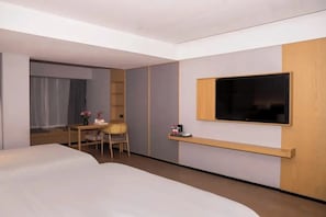 Habitación de hotel con cama, escritorio con silla, televisor montado en la pared y ventana con cortinas.