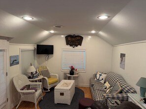 A cozy room with a television, wicker furniture, a sofa with checkered cushions, and a sign that reads 'Week-End Social Club.'