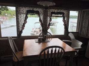 A dining area with a table and chairs, a lamp, and a view of a lake with boats and a flag.