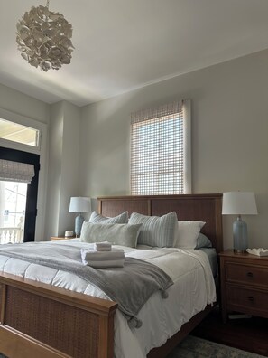 Een slaapkamer met een bed, nachtkastjes, een hanglamp, een raam met zonwering en uitzicht op buiten.