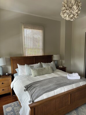 Een netjes opgemaakt bed met kussens, een nachtkastje met een lamp, een raam met uitzicht en een bijzondere plafondlamp.