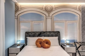 A bedroom with a tufted headboard, two bedside lamps, and a view of the sea through arched windows. - Sanità Naples Central Grand Apartment (Naples)