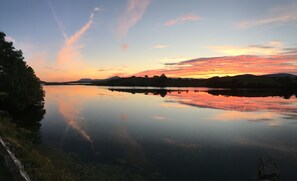 Un lac paisible qui reflète le ciel au coucher du soleil, avec des collines qui se dessinent à l’horizon.