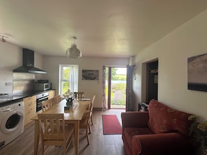 A kitchen with a microwave, stove, and washing machine; a dining table with chairs; a red sofa; and a door leading outside.