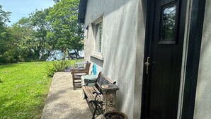 A house with a black door, a small window, a bench, a table, and a potted plant. - Cosy 2 bedroom  holiday apartment in a beautiful quiet area beside a lake. (Bantry)