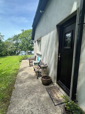 A house with a black door, a small window, a bench, a table, and a potted plant.