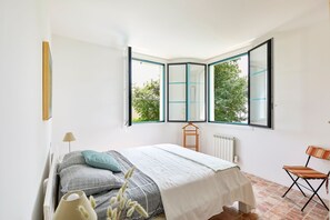 Ein Schlafzimmer mit Bett, Heizkörper, einem Fenster mit Vorhängen und einem Sessel.