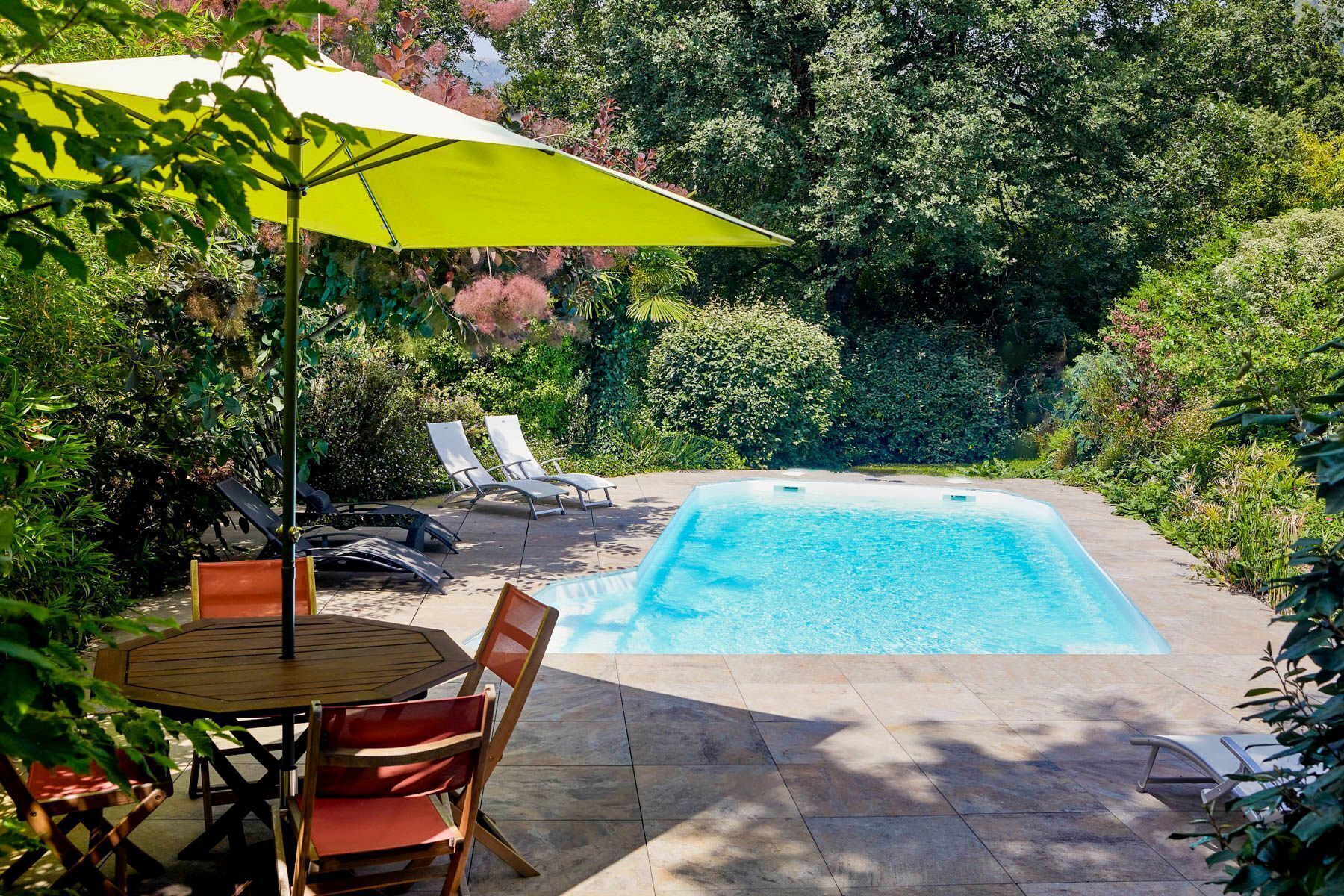 Piscina con sillas de descanso y una mesa, rodeada de vegetación.