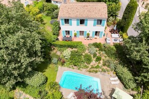 Ein zweistöckiges Haus mit Schwimmbad, umgeben von üppiger Vegetation und einer gepflasterten Terrasse.