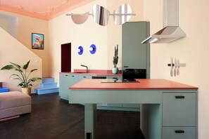 A modern kitchen with a large island, a dining area with a sofa, and a staircase leading to an upper level. - Poets Place Design Apartment II in Kreuzberg (Berlin)