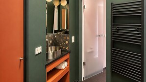 En hall med en dörr, en spegel, en handdukshängare och en bänkskiva med ett handfat.