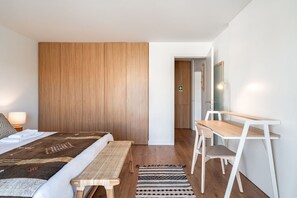 Ein Schlafzimmer mit Bett, Nachttisch, Bank, Schreibtisch, Stuhl und Spiegel.