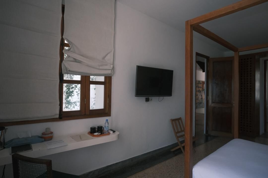 A bedroom with a bed, a TV mounted on the wall, a window with a view, a small table with items, and a chair.