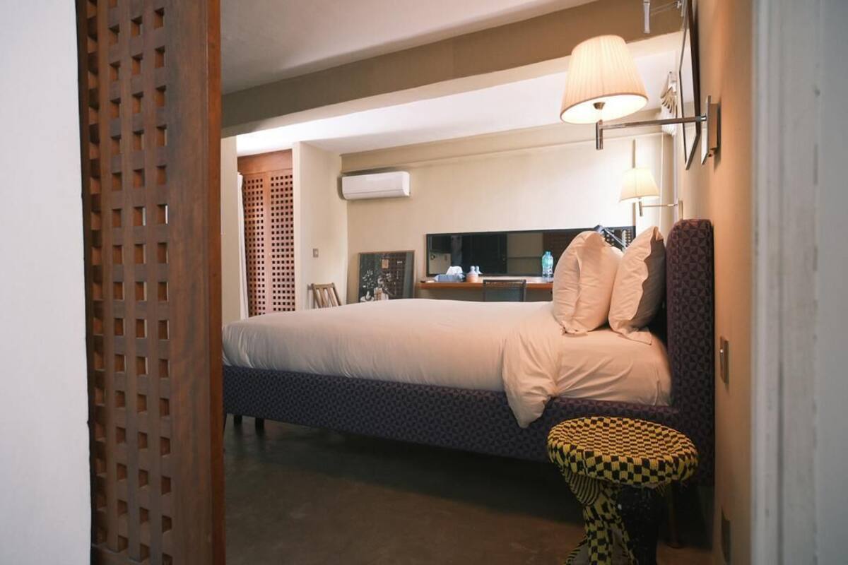 Una habitación de hotel con una cama, una mesita redonda pequeña, una lámpara de pared y un televisor.
