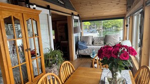 A wooden dining table with chairs, a glass cabinet with dishes, a sofa with pillows, and a vase with flowers. - STAY ABOVE THE WATER ON BEAUTIFUL LAKE WINNIPESAUKEE (Laconia)