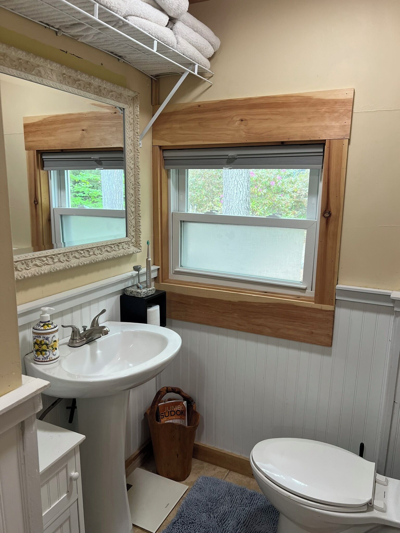 A bathroom with a white sink, a mirror, a window, and a toilet.