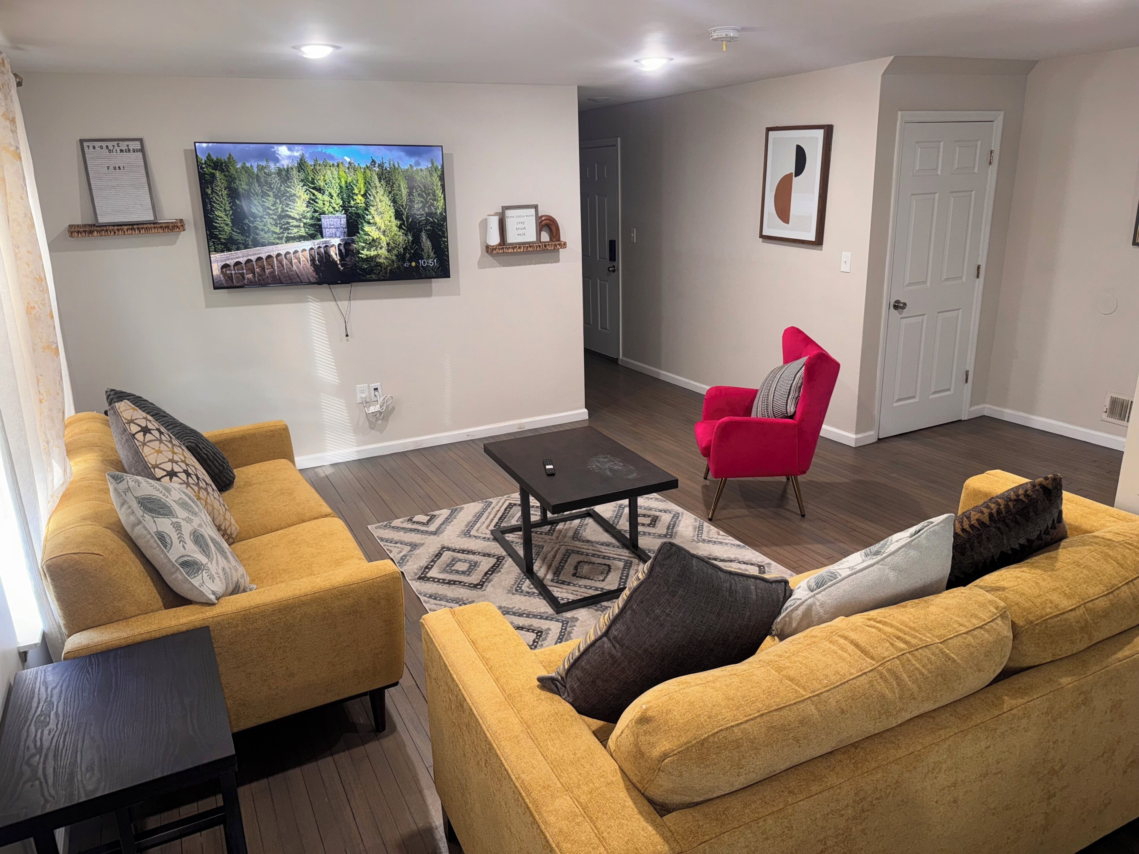 A living room with a sofa set, a coffee table, a red armchair, and a TV mounted on the wall.