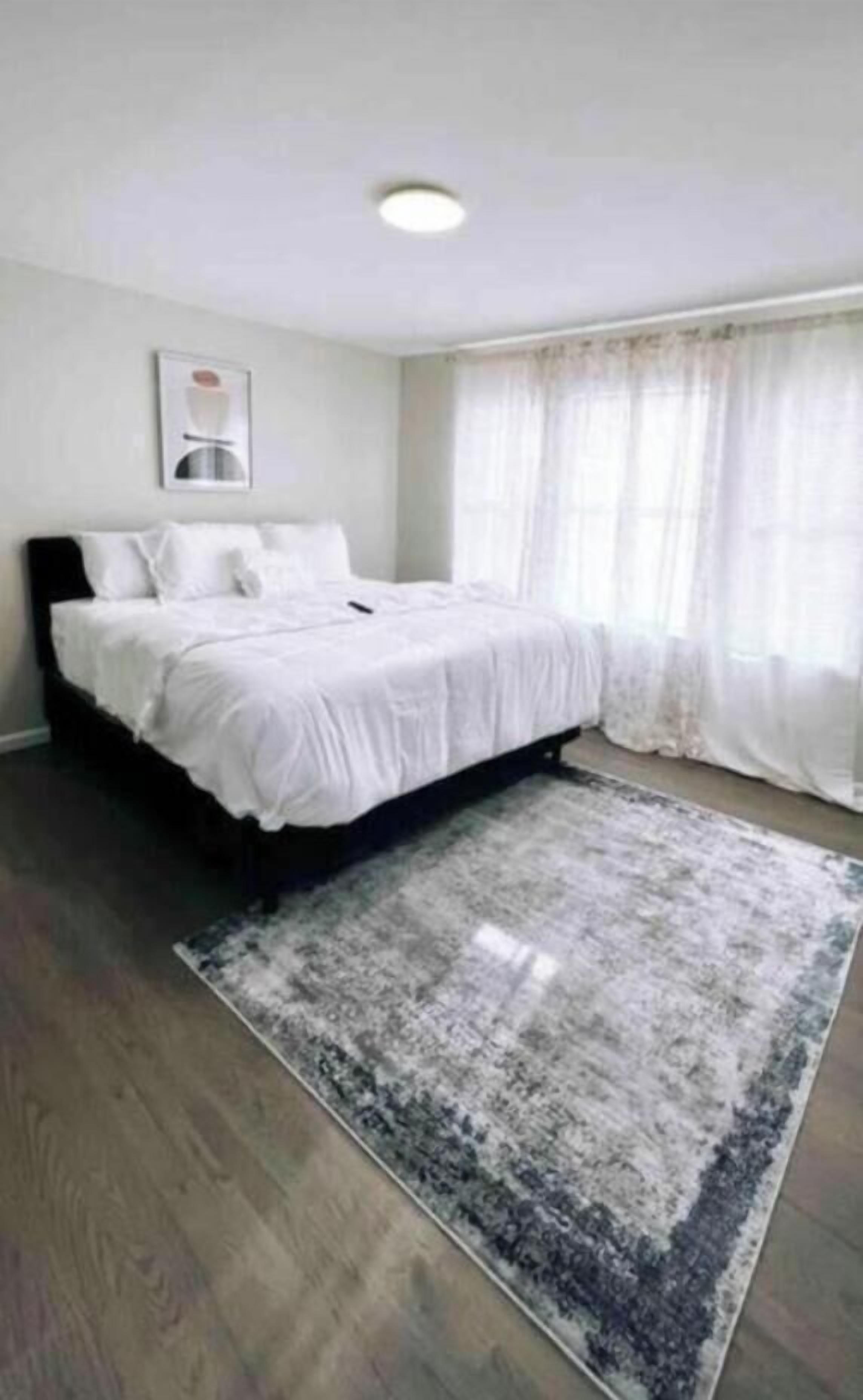 Un dormitorio con una cama, un tapete y una ventana con cortinas.