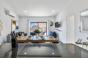 Un comedor moderno con una mesa dispuesta para cuatro, un ventanal con vista a edificios y un televisor montado en la pared.