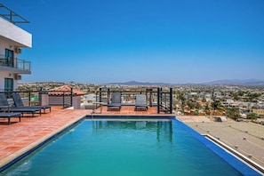Una piscina sul tetto con poltrone relax, un pergolato e vista sulla città.