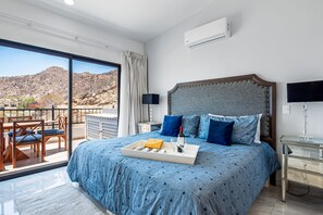 A hotel room with a large bed, a balcony with a view of the mountains, and a tray with a bottle and glasses on the bed. - Morgan Residences 607 @ Boutique Hotel With Pool, Gym & Spa (Cabo San Lucas)