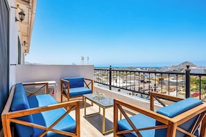 A balcony with blue cushioned seating, a small table, and a view of the city and mountains. - Morgan Residences 607 @ Boutique Hotel With Pool, Gym & Spa (Cabo San Lucas)