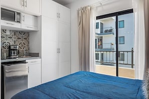 Una camera d'albergo con un letto, angolo cottura e un balcone che si affaccia sull'edificio.