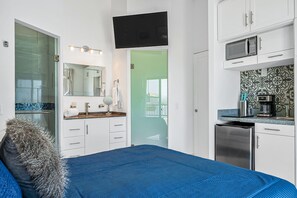 Quarto de hotel moderno com cama, banheiro e cozinha compacta.