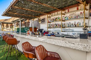 A bar area with a counter, bar stools, and shelves of bottles. - Morgan Residences 607 @ Boutique Hotel With Pool, Gym & Spa (Cabo San Lucas)