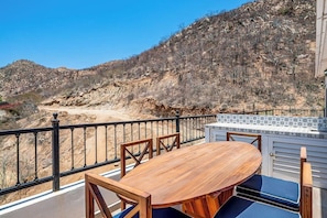 Una terrazza con tavolo e sedie in legno, zoccolo paraschizzi in piastrelle e vista su un pendio roccioso.