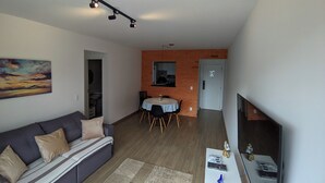 Ett modernt vardagsrum med en soffa, en matplats med stolar, en tv och en tegelvägg.