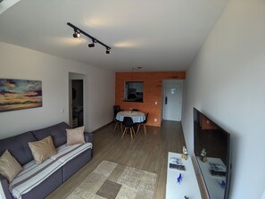 Ein modernes Wohnzimmer mit einer Couch, einem Essbereich mit Stühlen, einem Fernseher und einer Ziegelwand.