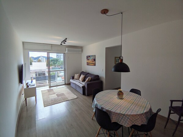 Ein Wohnzimmer mit einer Couch, einem Esstisch mit Stühlen, einem Fernseher und einem großen Fenster.
