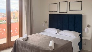 Habitación de hotel con cama, dos lámparas de noche, una ventana con cortinas y vista a edificios.