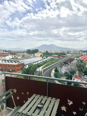 Un balcone con vista sulla città, una montagna all'orizzonte e una strada con dei veicoli.