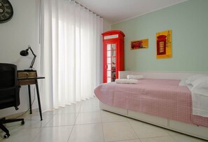A bedroom with a bed, a desk, a chair, a red telephone booth, and two wall art pieces.
