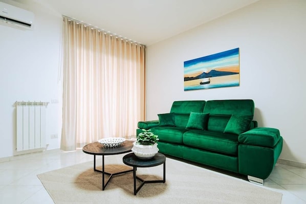 A living room with a green sofa, a painting of a landscape, and a radiator.