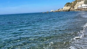 A coastal beach with clear water, rocky shore, and buildings on the cliff. - SEA VIEW apartment OCEAN Cava dell'isola • Elowen (Forio)